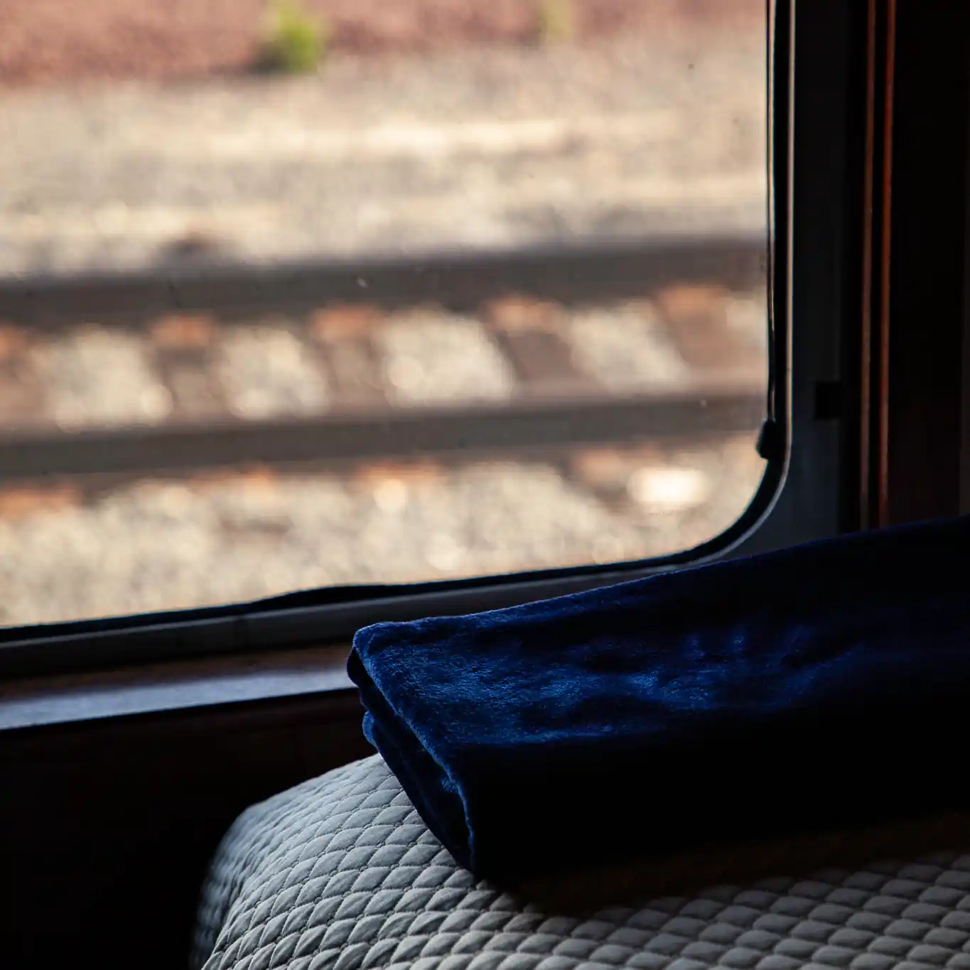 A photograph of a private railcar bedroom with train tracks visible through the window